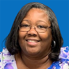 Woman with glasses smiling, wearing a floral blouse, against a blue background.
