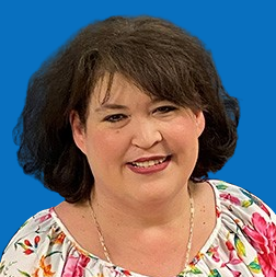 Blonde woman smiling, wearing a beige and white zebra-striped turtleneck, against a blue backdrop.