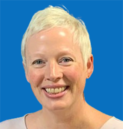 Woman with short blonde hair smiles, wearing patterned top and earrings, against a blue background.