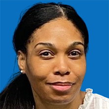 Blonde woman with blue eyes smiles, wearing a pink shirt, in front of a teal background.