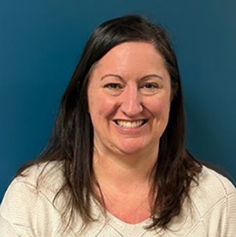 Woman with long brown hair smiling at the camera, wearing a black turtleneck against a blue background.