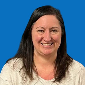 Woman with long brown hair smiling at the camera, wearing a black turtleneck against a blue background.
