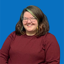 Person with dark hair, glasses, and nose piercing smiles at camera, green highlights.