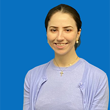 Woman with brown hair smiling, wearing pearl earrings, against a blue background.