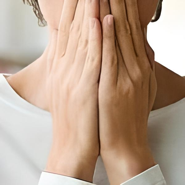 Person with hands covering their face, showing distress. White shirt and setting.