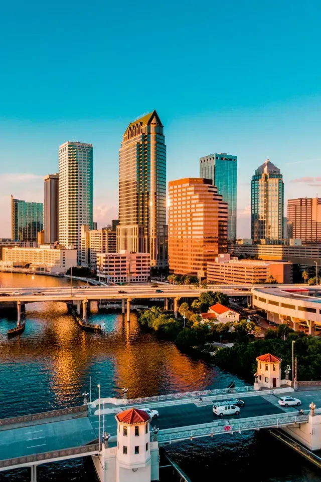 A vibrant skyline of Tampa, Florida, with modern skyscrapers reflecting on the water, under a clear blue sky.