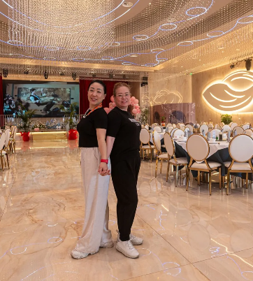 Due donne sono in piedi una accanto all'altra in una grande stanza con tavoli e sedie.