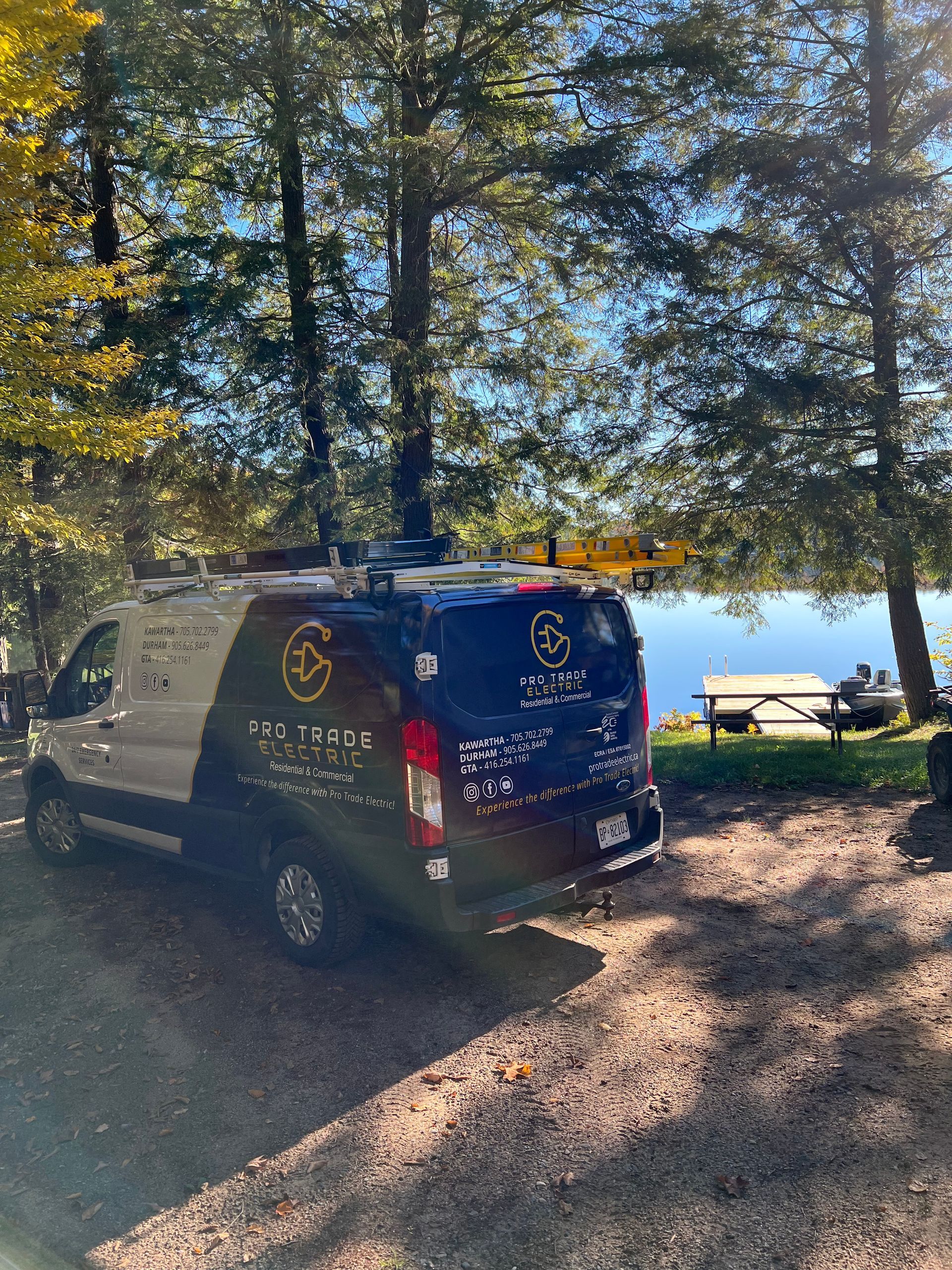 A van is parked in a gravel lot next to a lake.