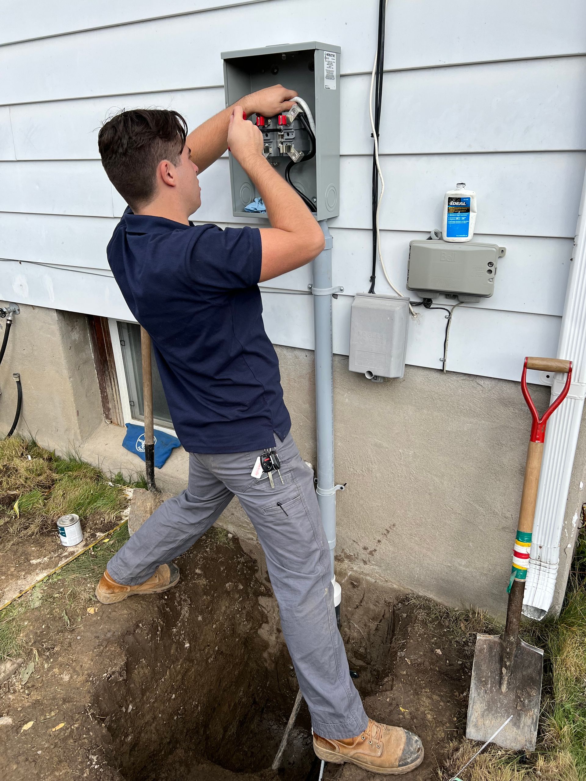 A man is working on an electrical box on the side of a house.