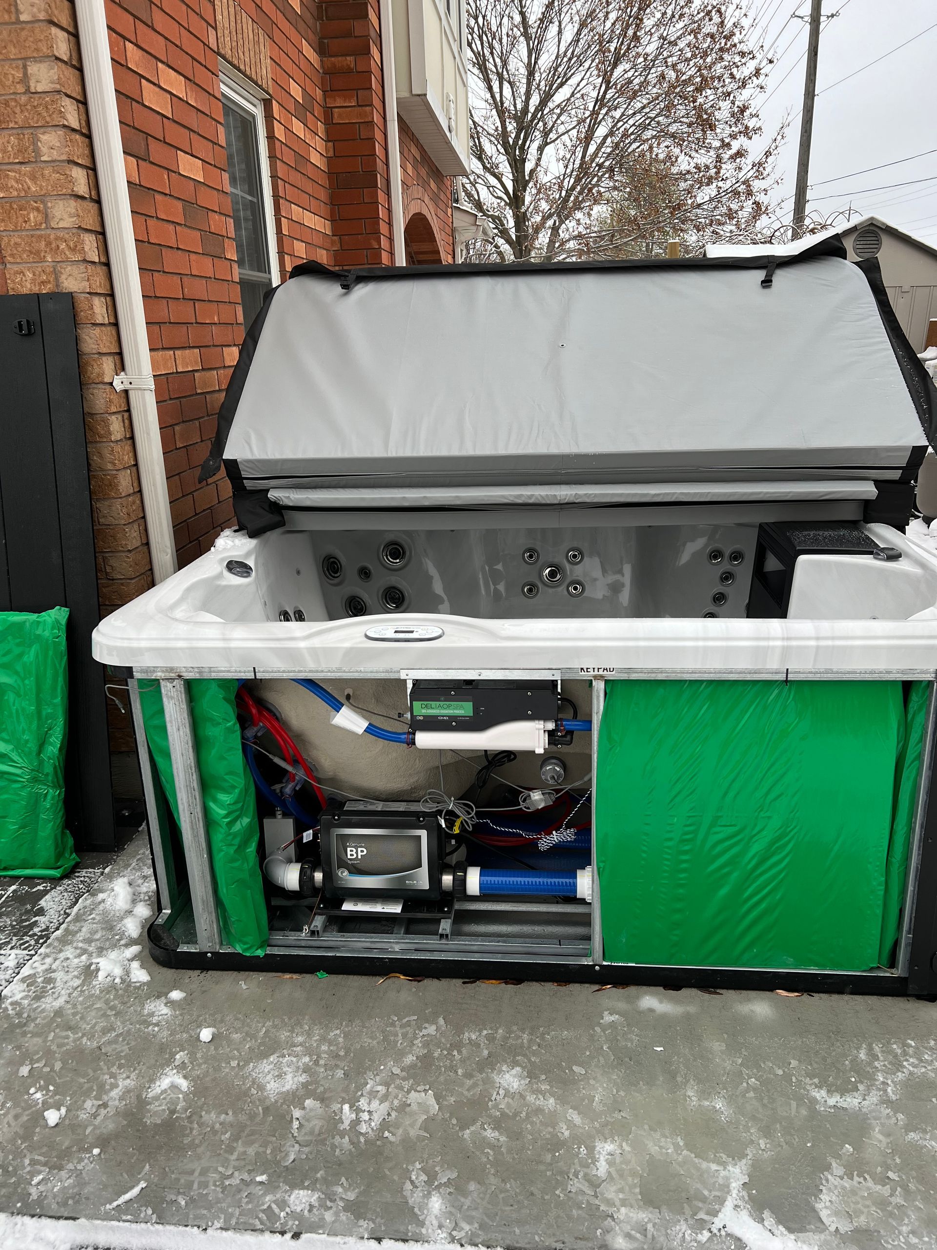A hot tub with the lid open is sitting in front of a brick building.