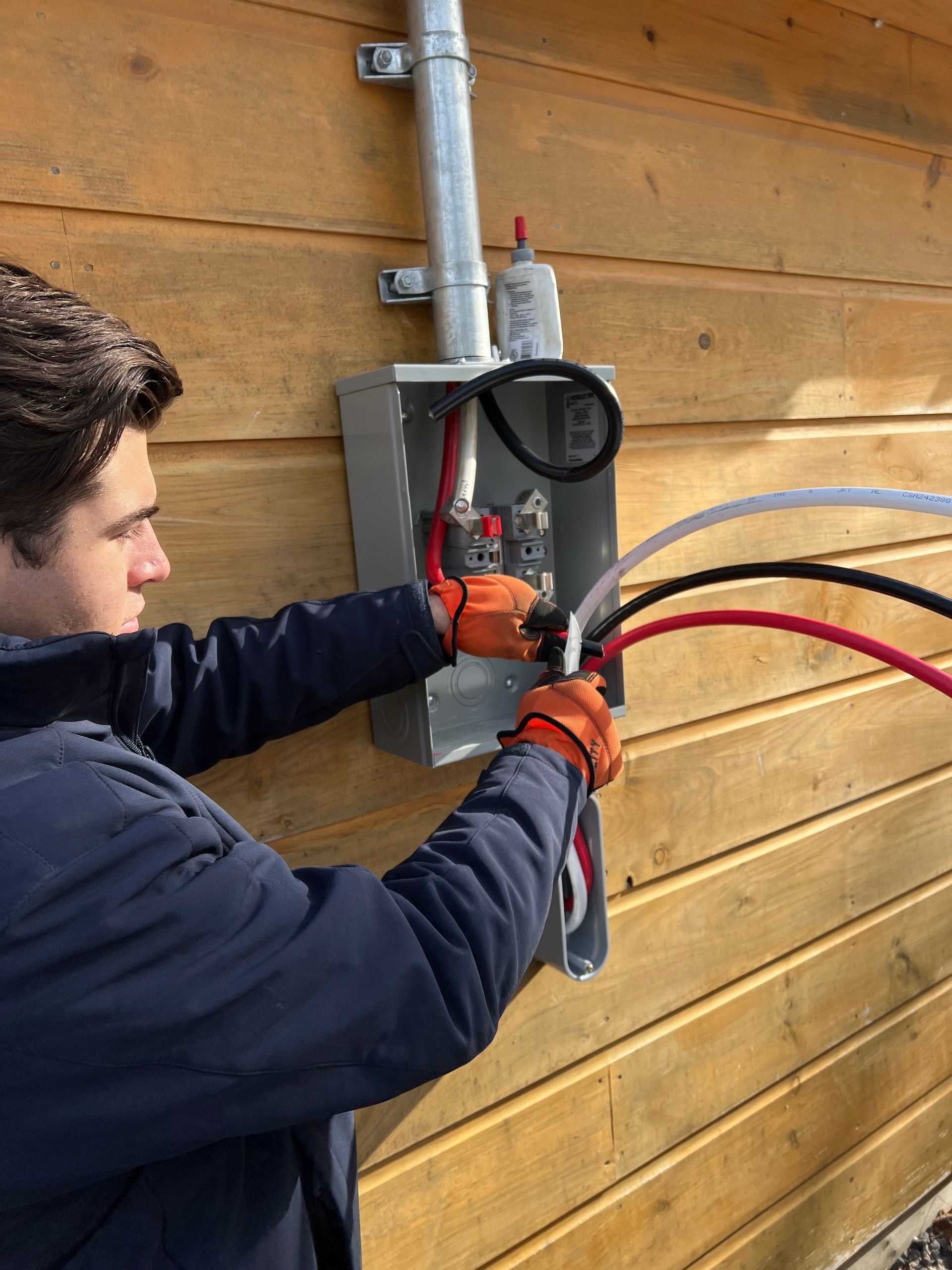 A man is working on an electrical box on a wooden wall.