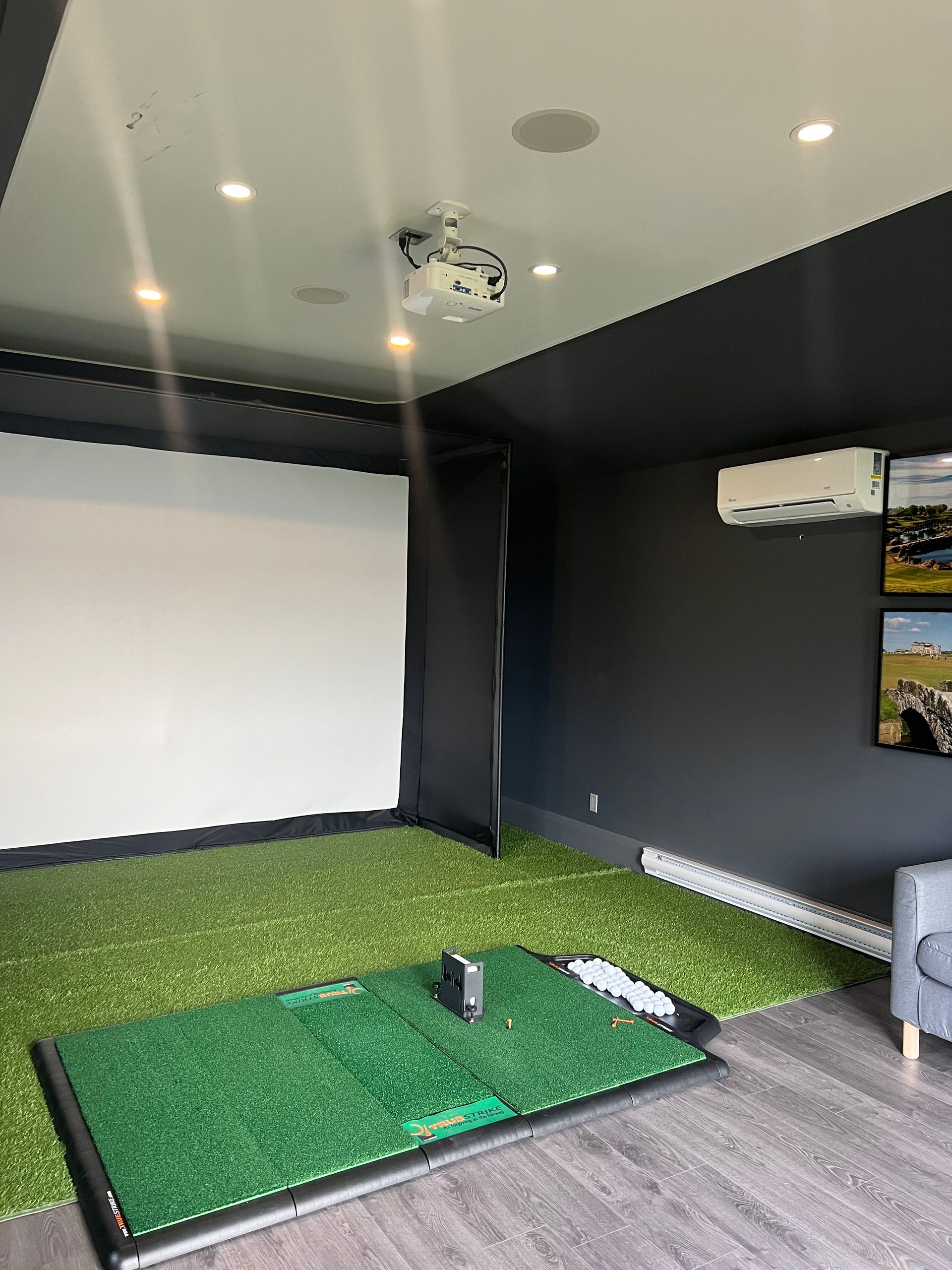 A living room with a projector screen and a golf mat.