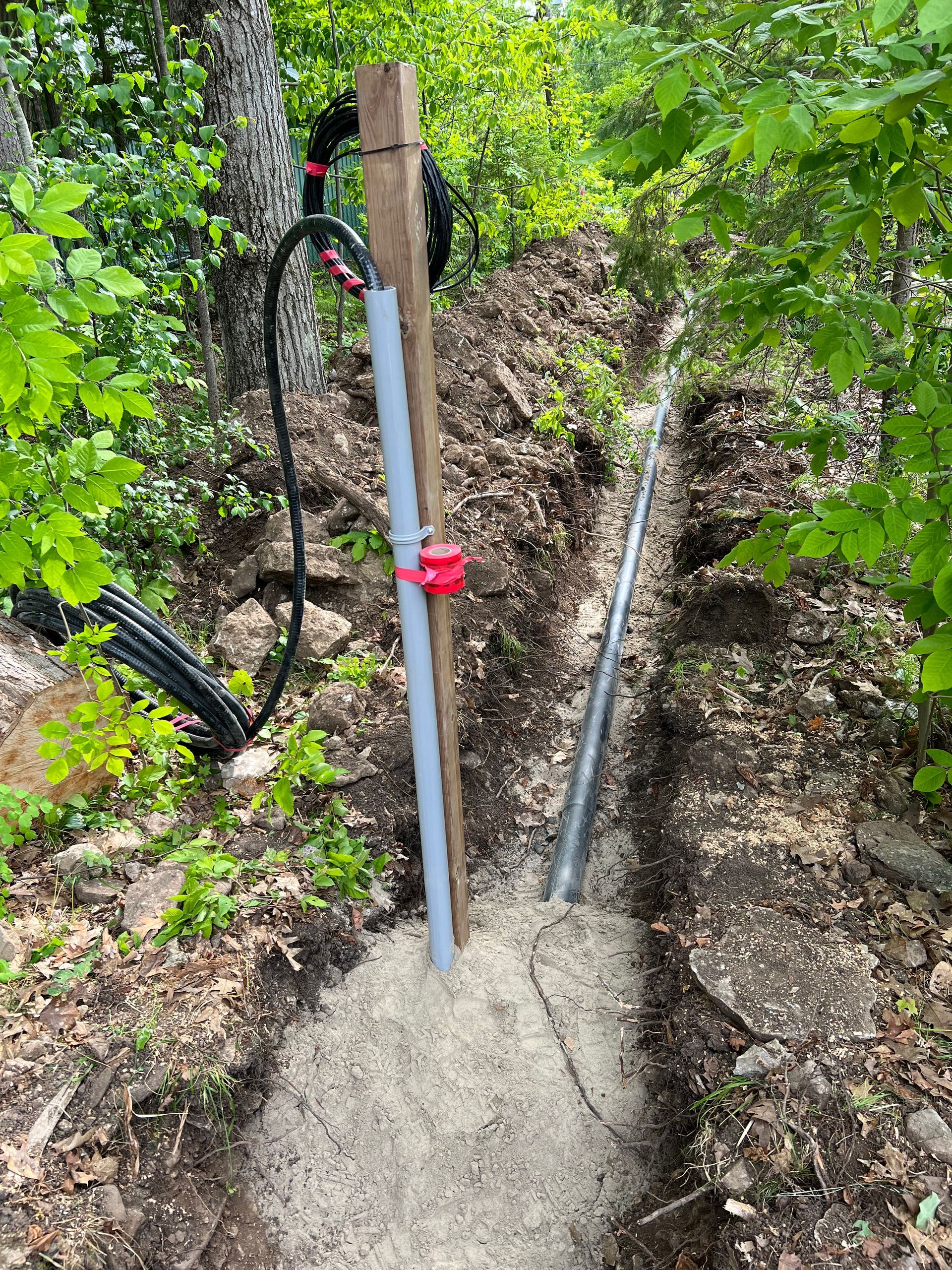 A pipe is being installed in a trench in the woods.
