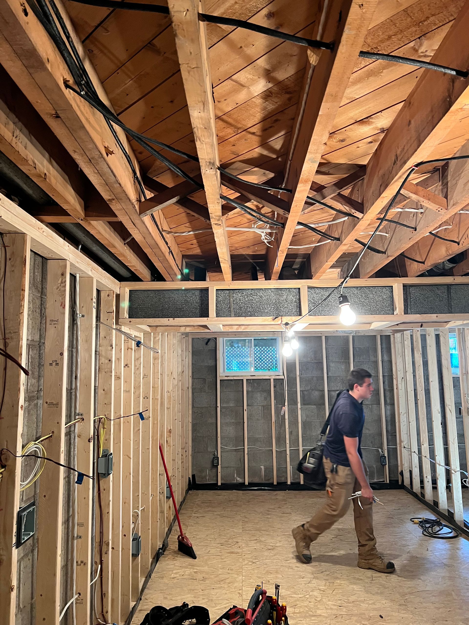 Man working on framing for a room. Wooden beams and walls are visible, along with electrical wiring.