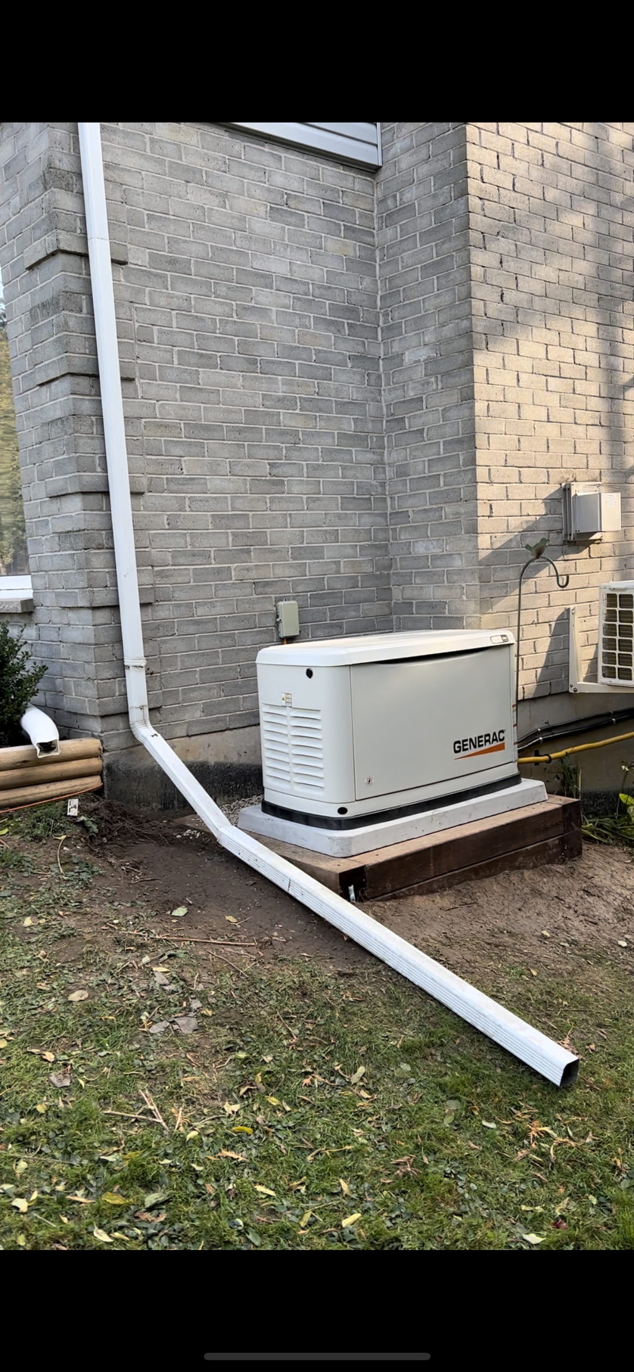 A generator is sitting on the side of a house next to a drain pipe.