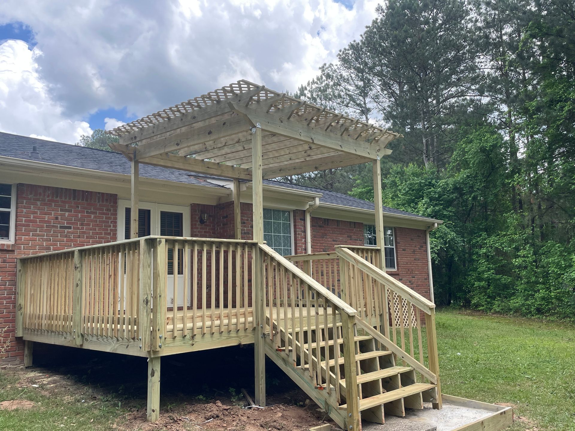 A wooden deck with stairs and a pergola is in front of a brick house.