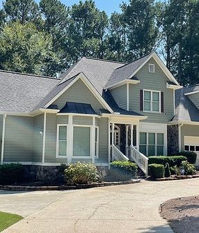 A large house with a gray roof and white trim is surrounded by trees.