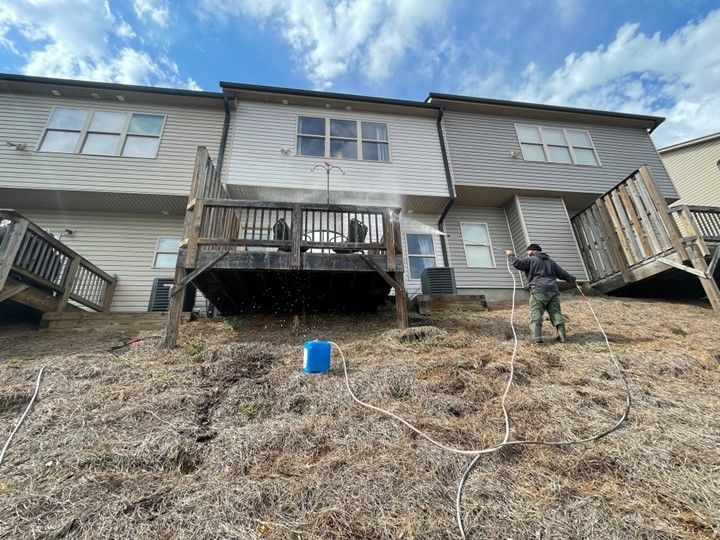 A man is cleaning the back of a house with a pressure washer.