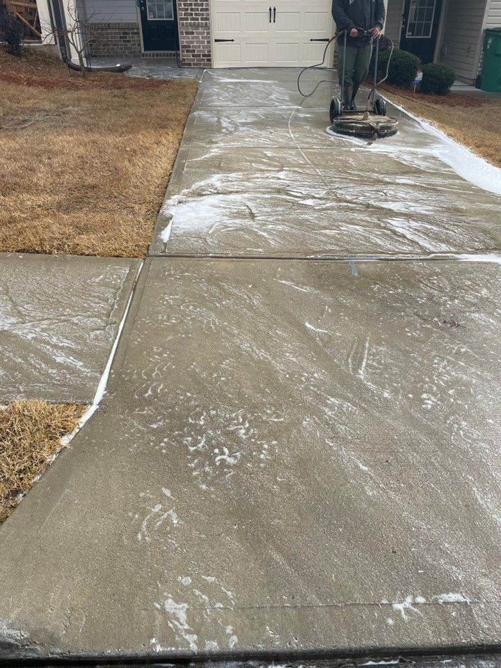 A man is cleaning a concrete driveway with a machine.
