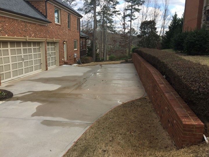 A brick wall surrounds a concrete driveway in front of a brick house.