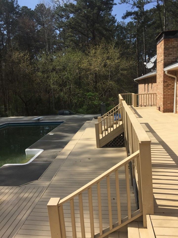 A wooden deck with stairs leading to a swimming pool surrounded by trees.