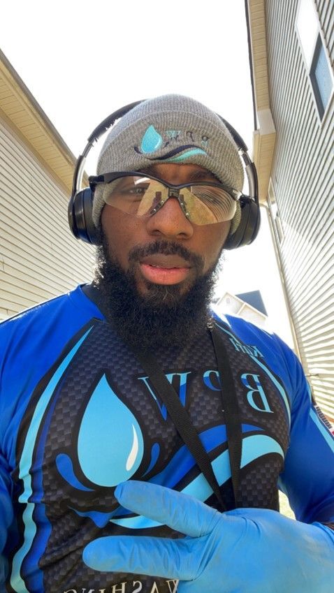 A man wearing headphones , glasses and a blue shirt is standing in front of a building.