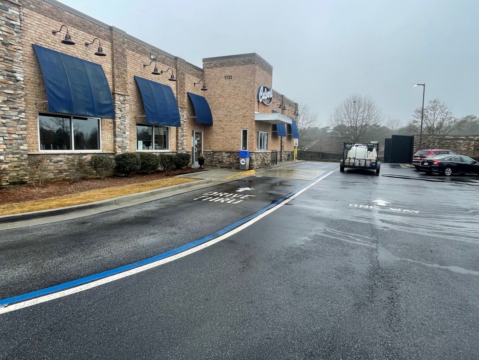 A brick building with blue awnings and a parking lot in front of it.