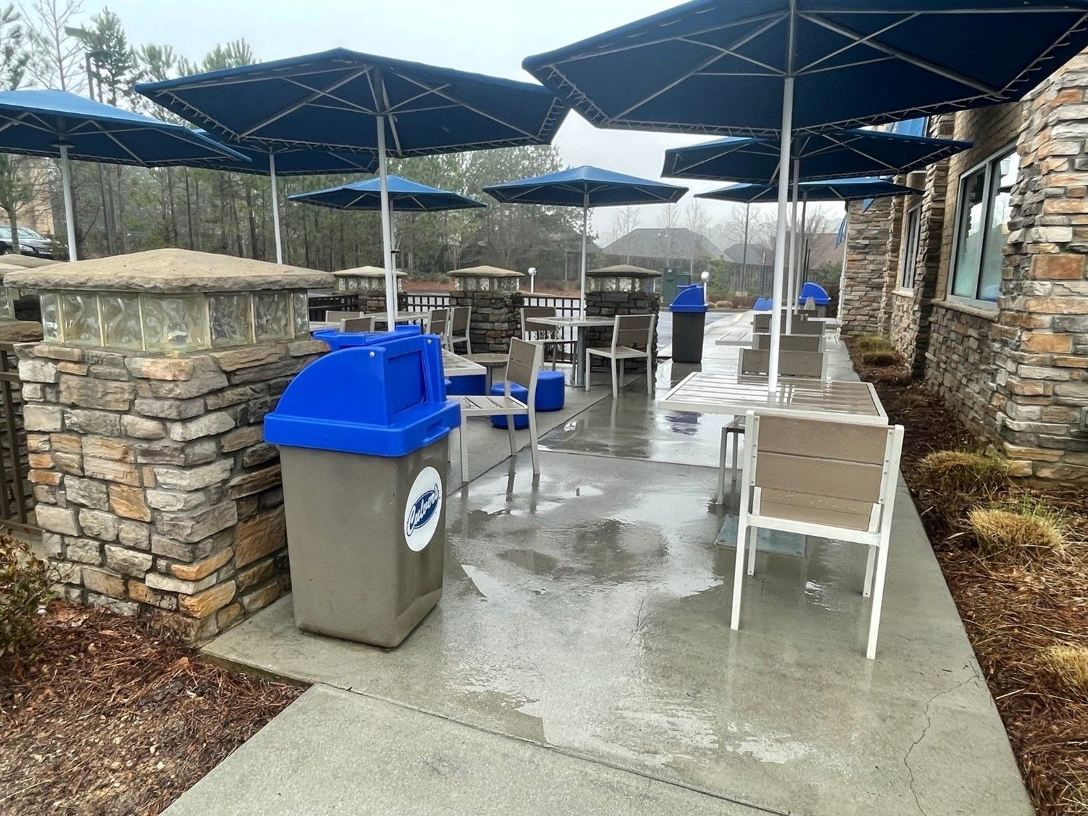 A patio with tables and chairs and umbrellas on a rainy day.