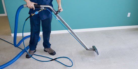 Man using a water extraction vacuum to remove moisture from a carpeted floor.