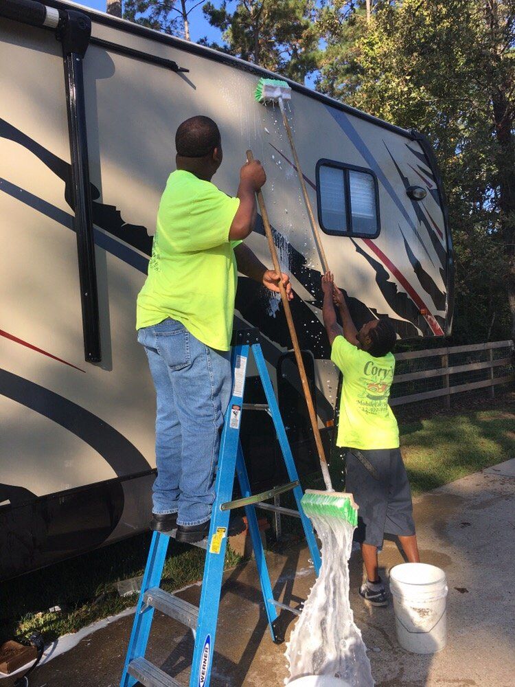 Two men standing on a ladder cleaning a rv