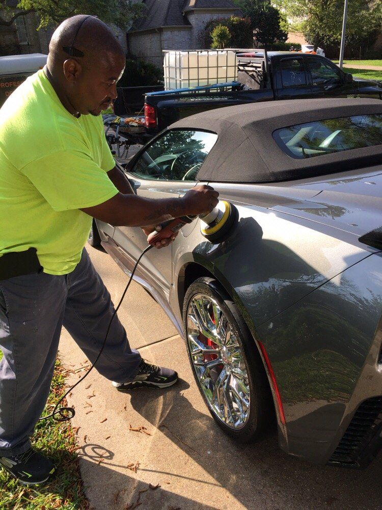 A man in a neon yellow shirt is polishing a car