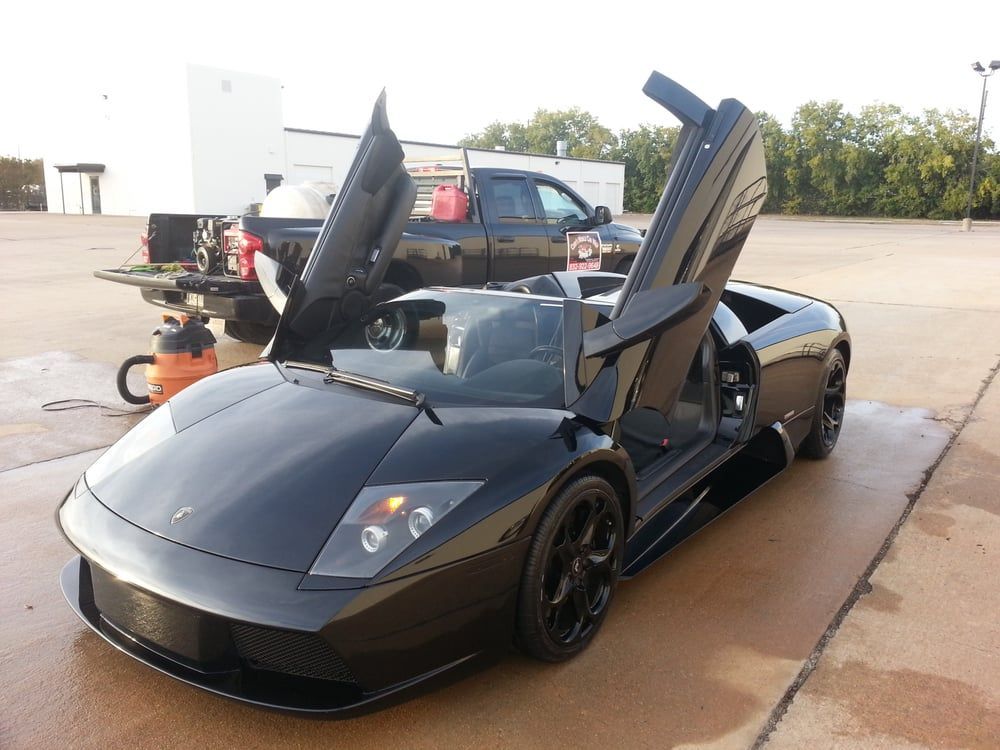 A black sports car is parked in a parking lot with its doors open