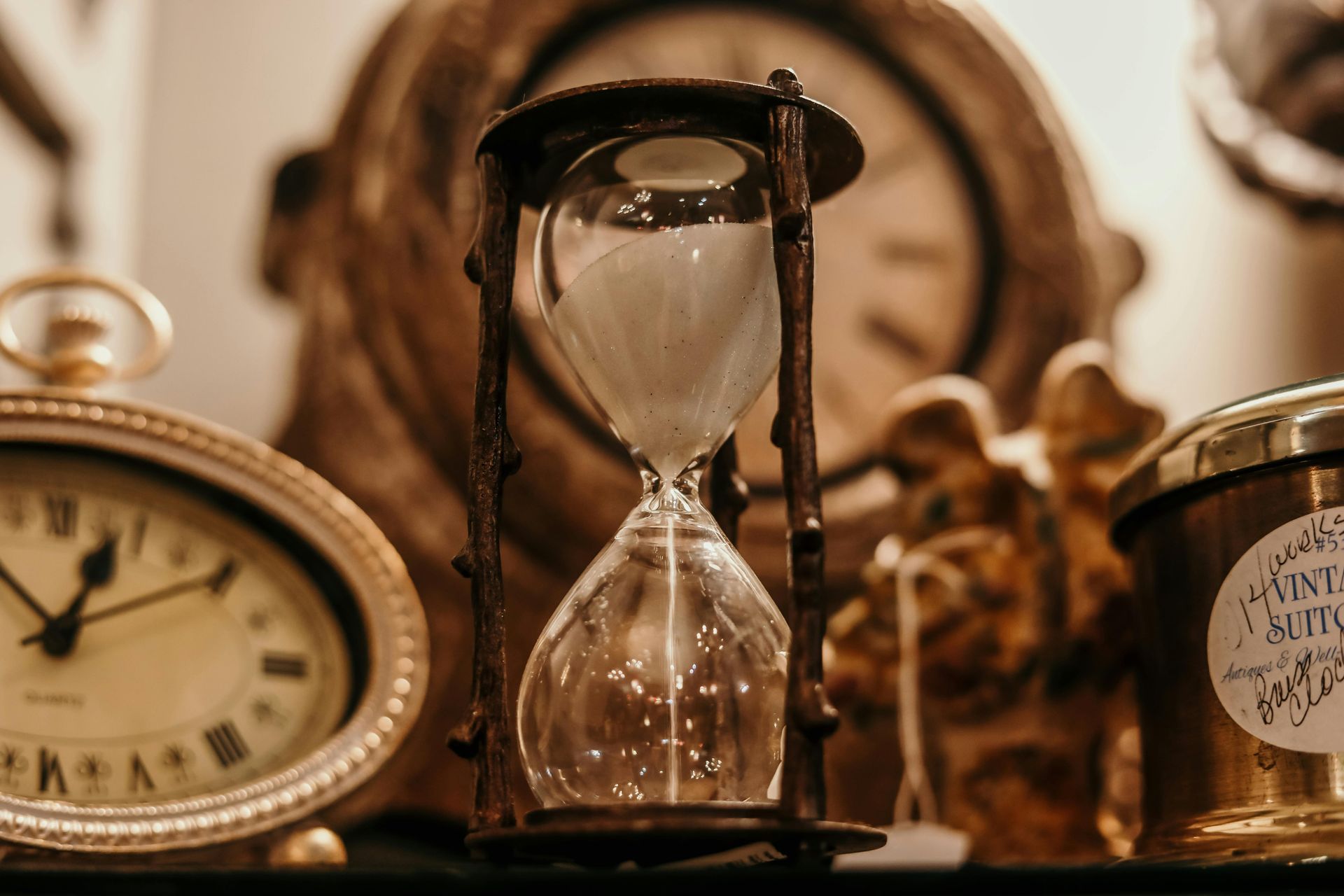 Hourglass with sand draining, surrounded by antique clocks.