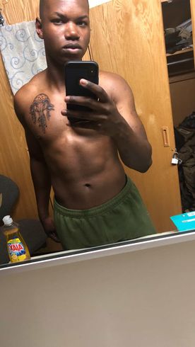 A person shirtless, with a tattoo on their chest, holding a phone in front of a bathroom mirror.