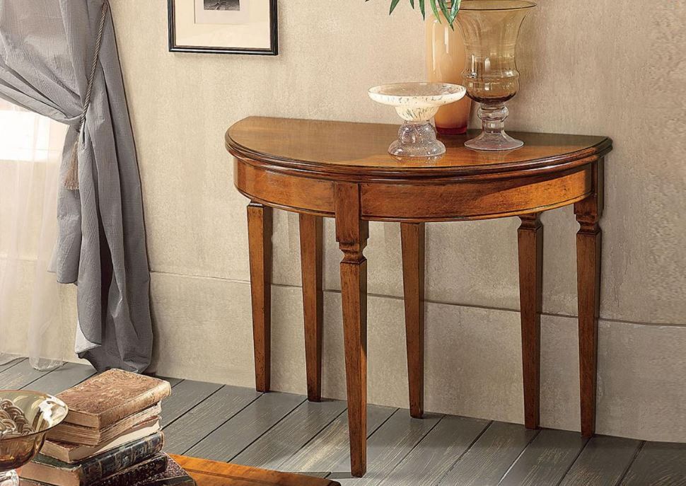 Tavolo in legno a forma di mezzaluna appoggiato a una parete, sormontato da vasi di vetro.