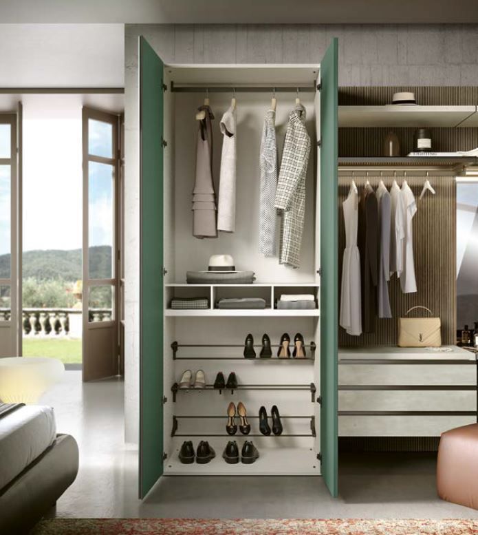 Moderno armadio con porta verde, vestiti appesi, scarpiere e porta aperta su un balcone.