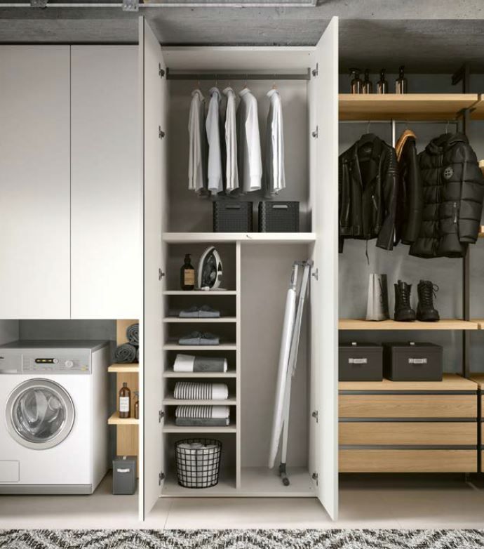Lavanderia con mobili bianchi, lavatrice e armadio a muro aperto con vestiti e spazio per riporre gli oggetti.