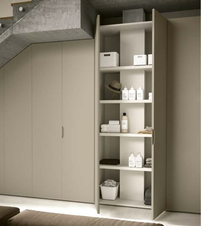 Scaffale alto e aperto con prodotti per la pulizia e asciugamani accanto a un ripostiglio chiuso sotto una scala.
