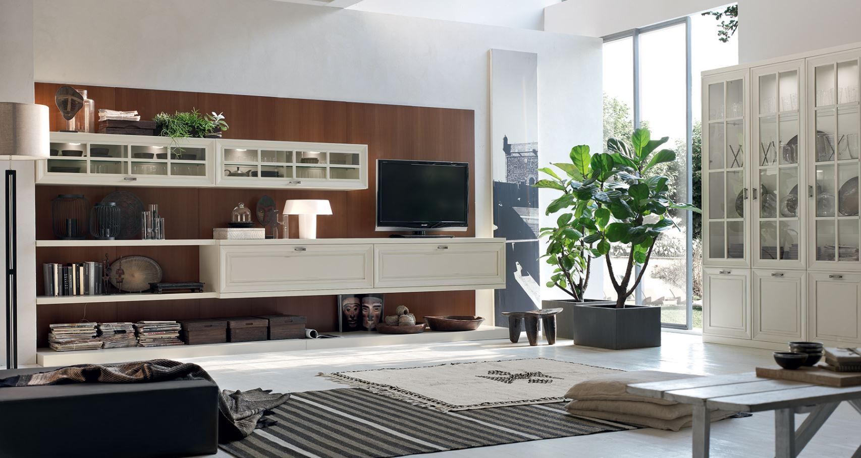 Soggiorno moderno con parete attrezzata in legno, TV e grande pianta. Mobili bianchi e luce naturale.