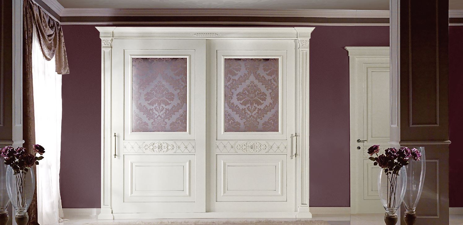 Armadio bianco con ante in vetro decorato in una stanza con pareti viola scuro, una porta e vasi.