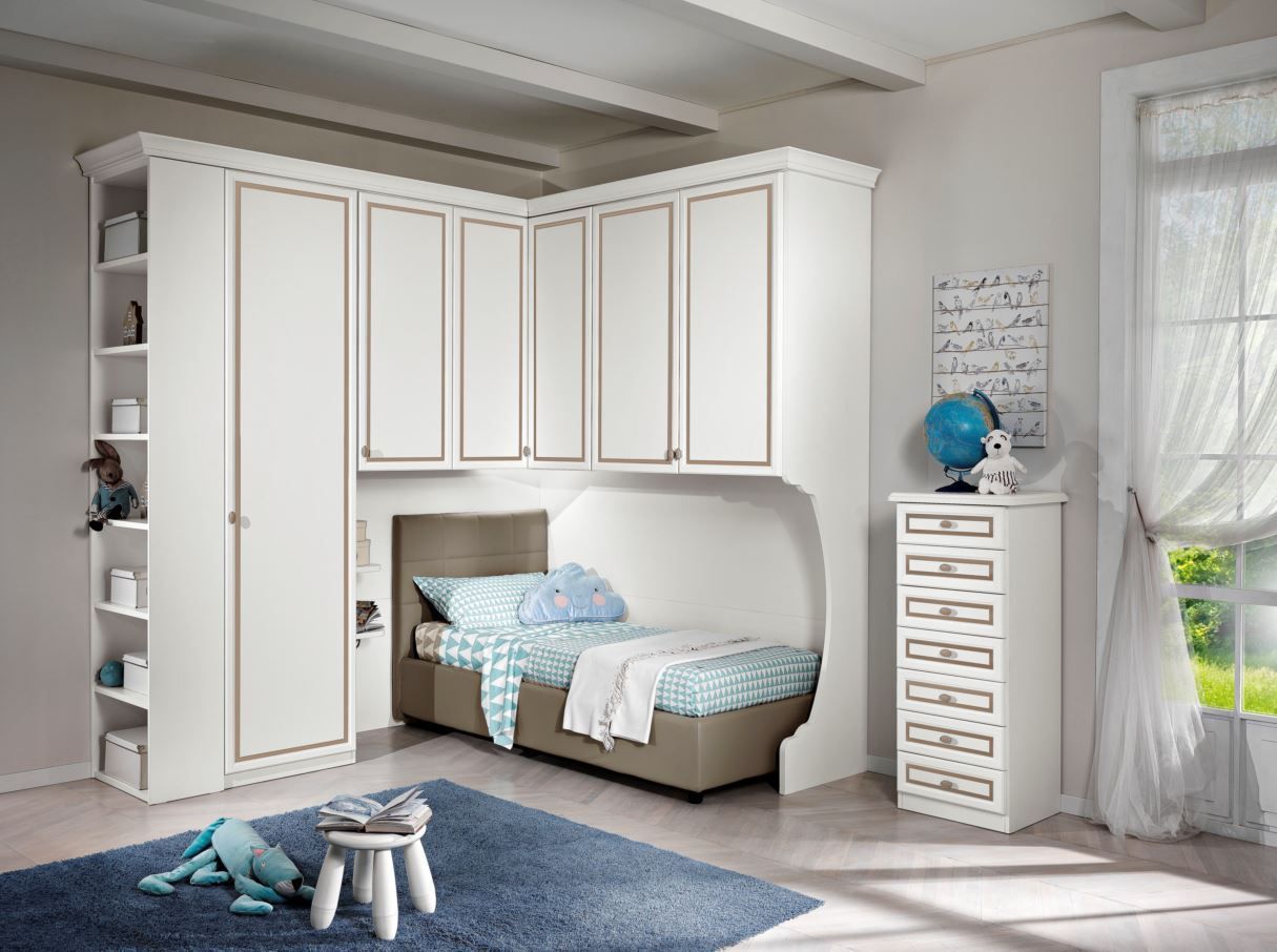 Cameretta per bambini con armadi bianchi a muro, letto, cassettiera e tappeto blu. Stanza luminosa con luce naturale.