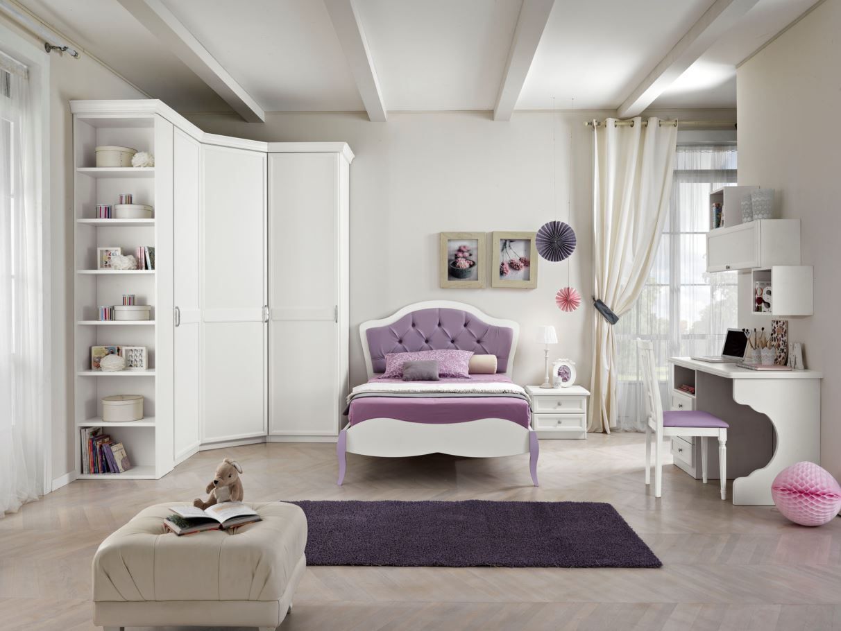 Camera da letto per bambina con mobili bianchi, letto viola, scrivania e tappeto. Spazio luminoso e arioso, decorato con motivi floreali.