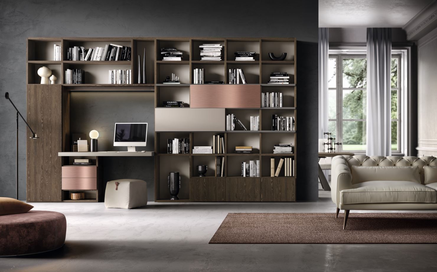 Soggiorno con scrivania integrata, librerie, divano e colori neutri; la luce naturale entra da una finestra.