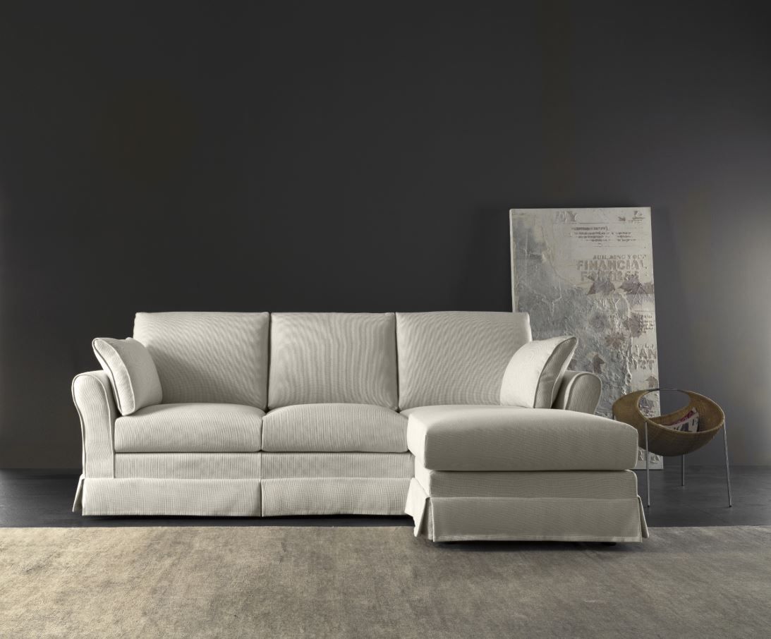 Divano componibile color crema con chaise longue contro una parete grigio scuro, opere d'arte astratte e poltrona laterale.