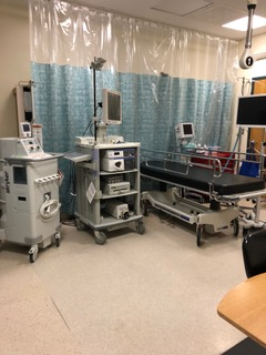 A hospital room with a bed , carts , monitors and other medical equipment.