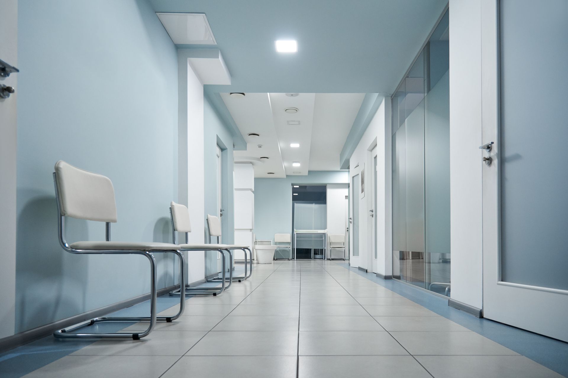 A long hallway in a hospital with chairs and doors.