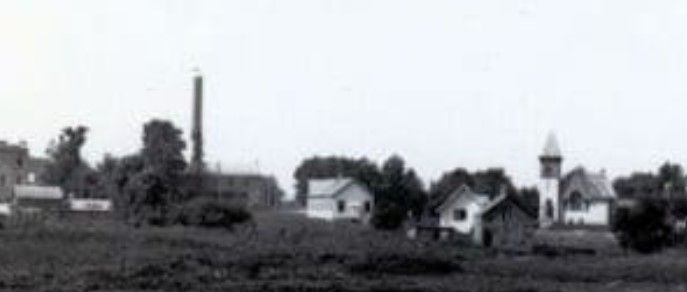 A grayscale photo of a small town with buildings, trees, and a church.