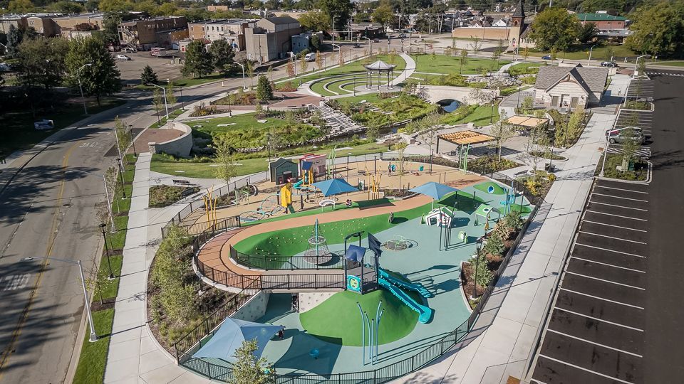 Aerial view of park with playground, gardens, walking paths, and parking lot.