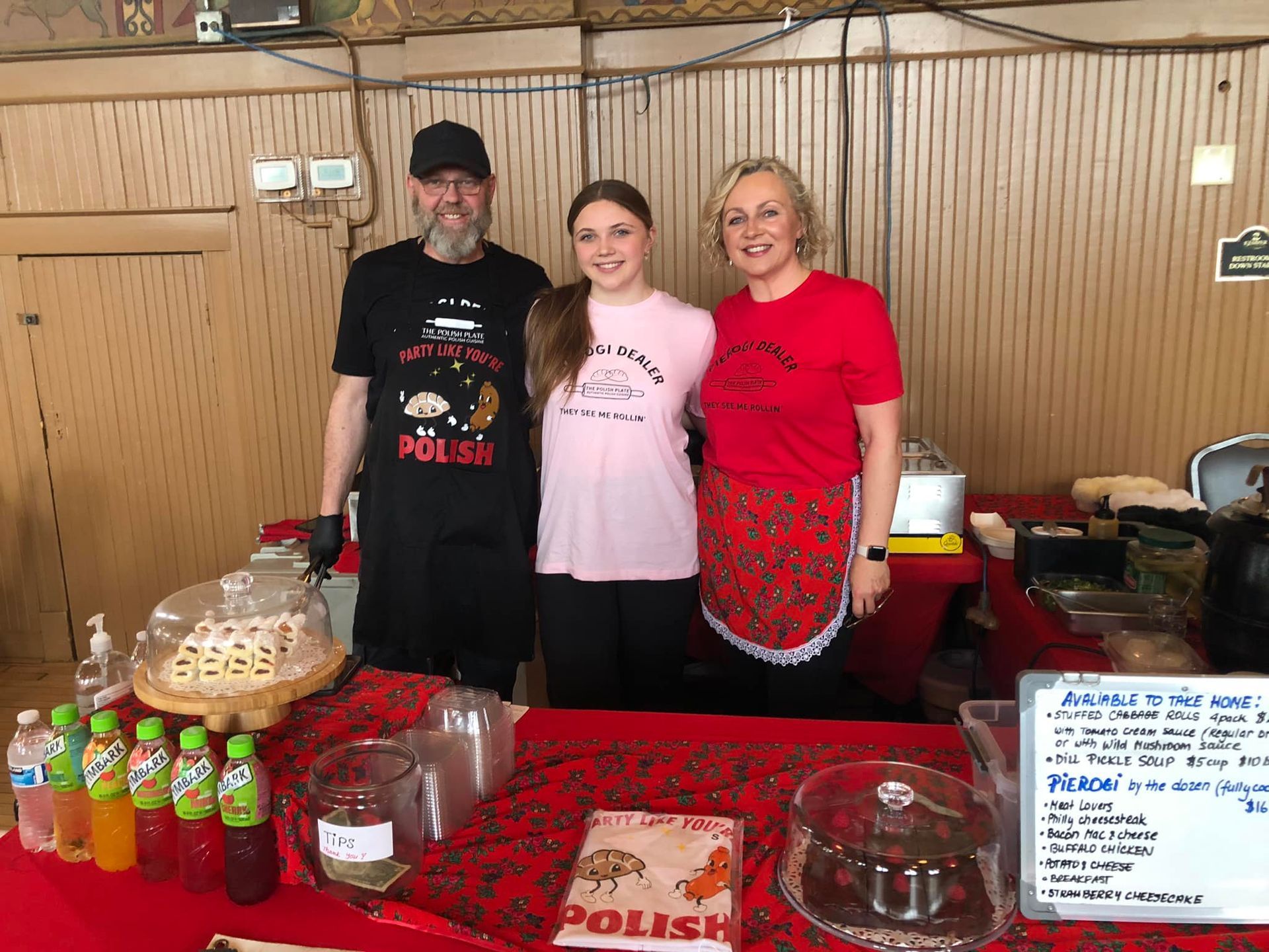 Three people stand behind a food stall with Polish treats and drinks.