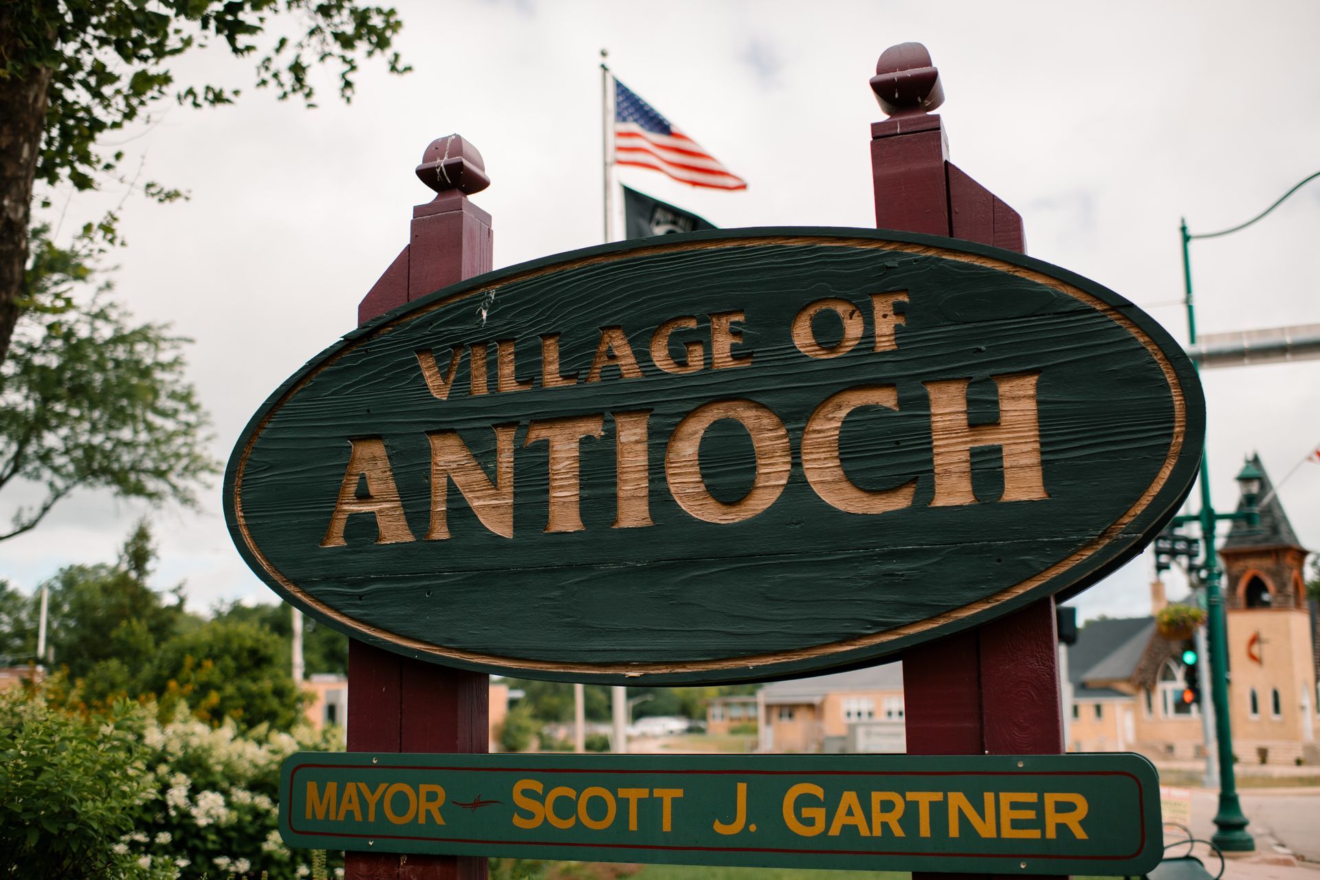 Village of Antioch sign with American flag, brown and green, with mayor's name.